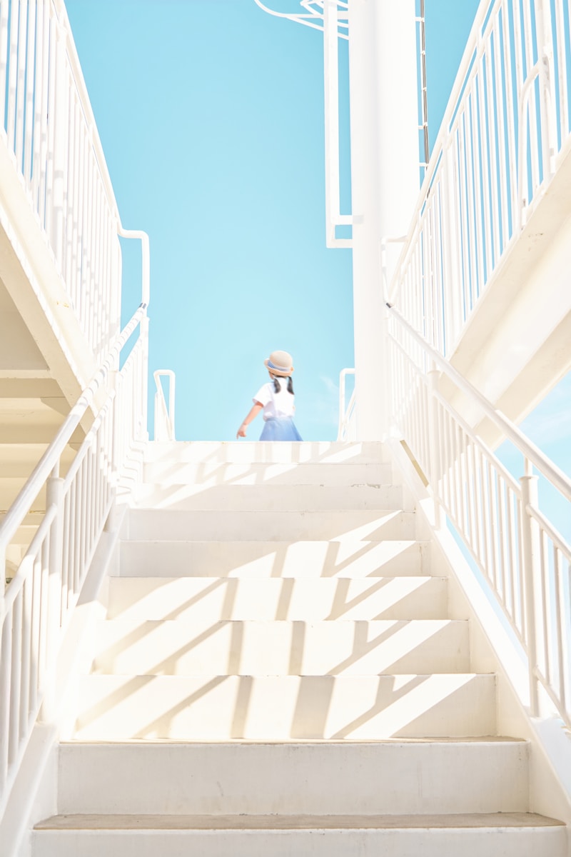 A girl climbs white stairs into the bright sky.